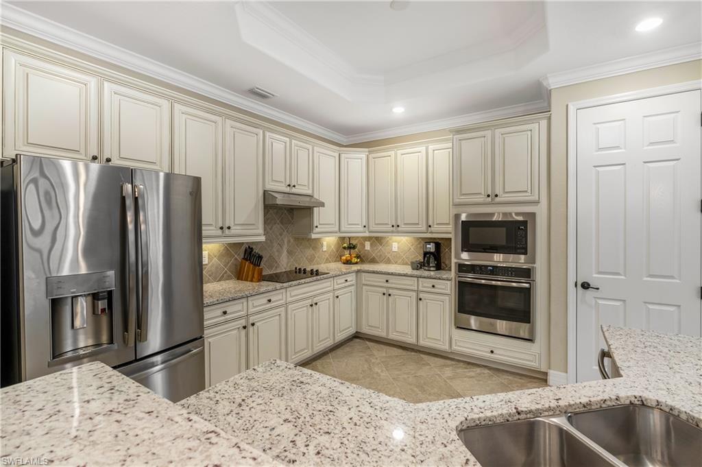 Kitchen featuring stainless steel appliances, cream cabinetry, crown molding, light stone counters, and recessed lighting
