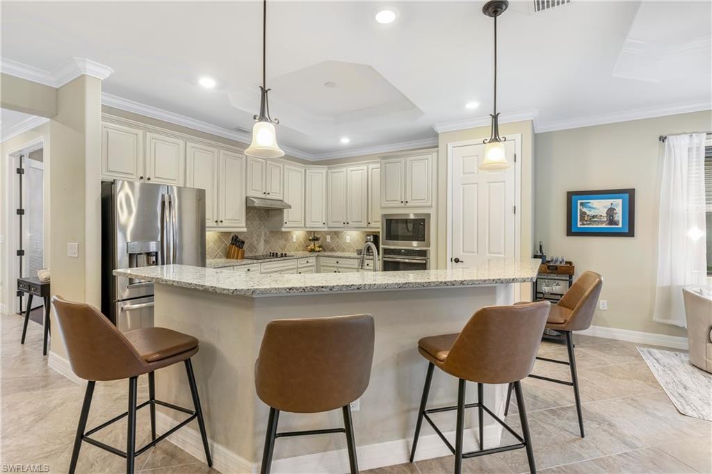 Kitchen with backsplash, a kitchen bar, light stone countertops, ornamental molding, and stainless steel appliances