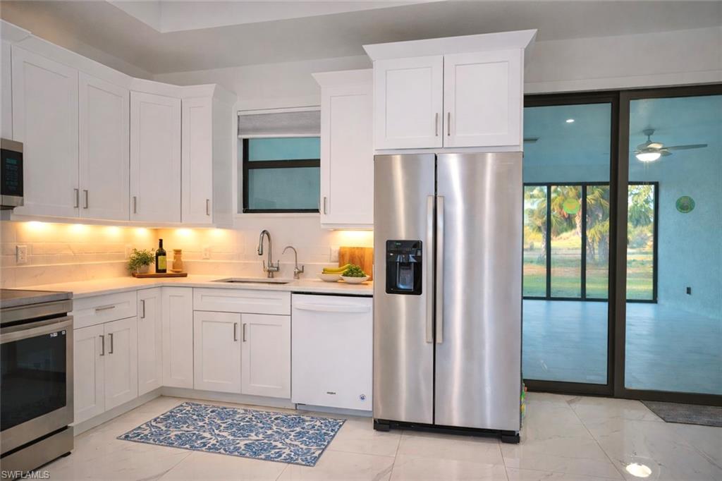Kitchen featuring stainless steel appliances, white cabinets, light stone countertops, decorative backsplash, and a ceiling fan