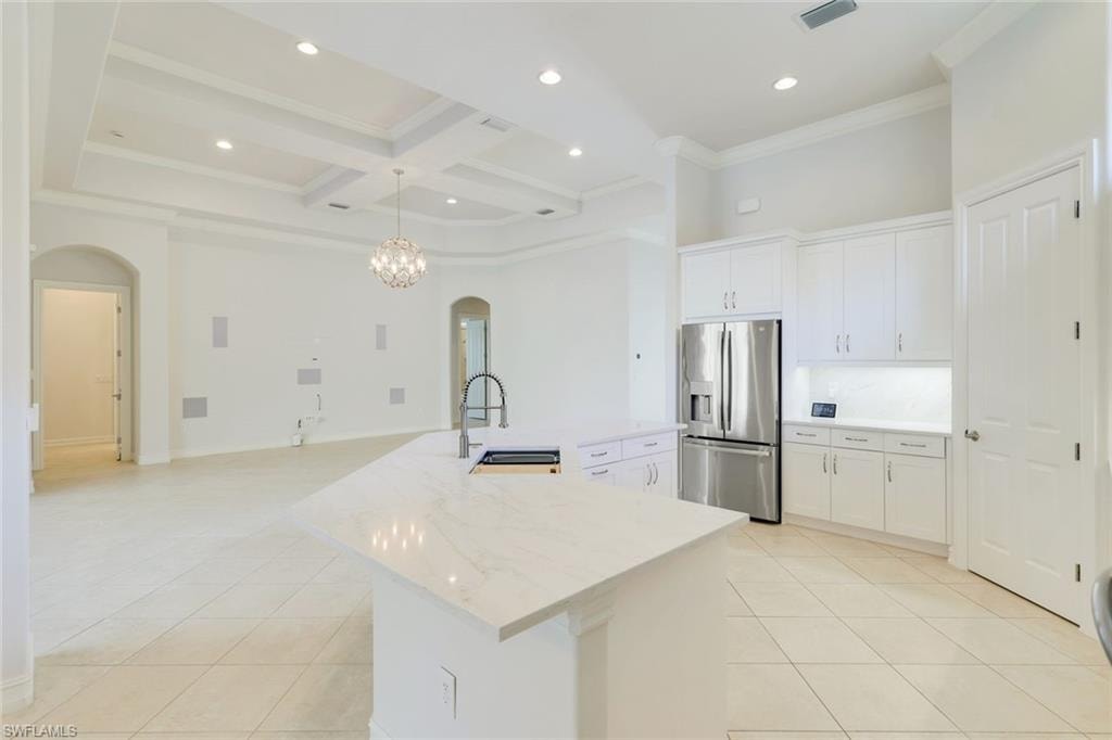 Kitchen featuring arched walkways, white cabinetry, stainless steel refrigerator with ice dispenser, coffered ceiling, and a spacious island
