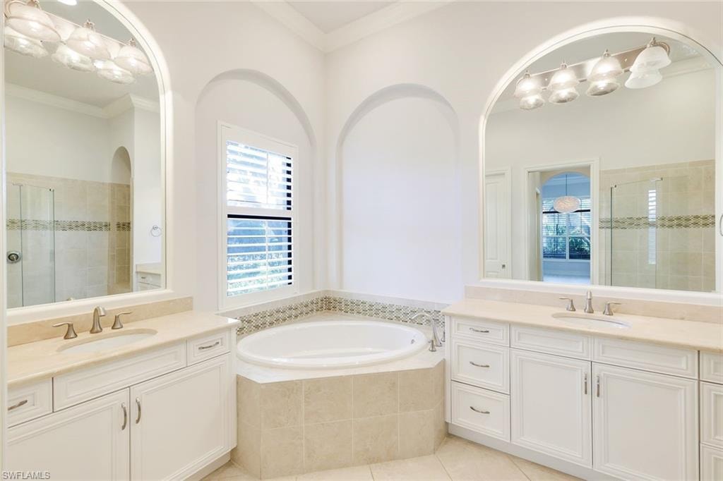Full bath with a stall shower, light tile patterned floors, two vanities, a garden tub, and crown molding