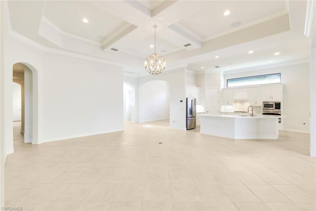 Unfurnished living room with arched walkways, coffered ceiling, ornamental molding, hanging lights, and light tile patterned floors
