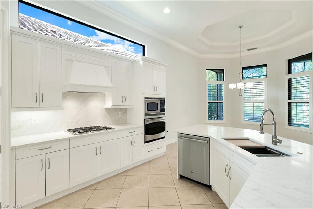 Kitchen featuring stainless steel appliances, light stone countertops, white cabinetry, crown molding, and light tile patterned floors