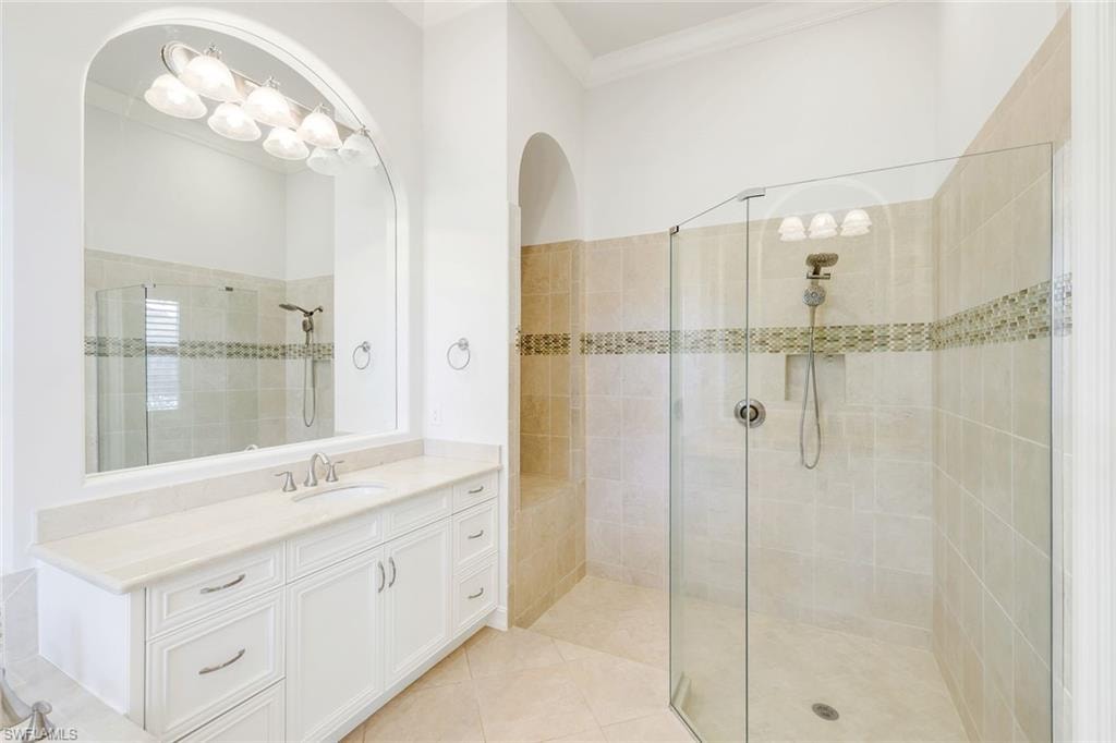 Bathroom featuring vanity, walk in shower, crown molding, and light tile patterned floors