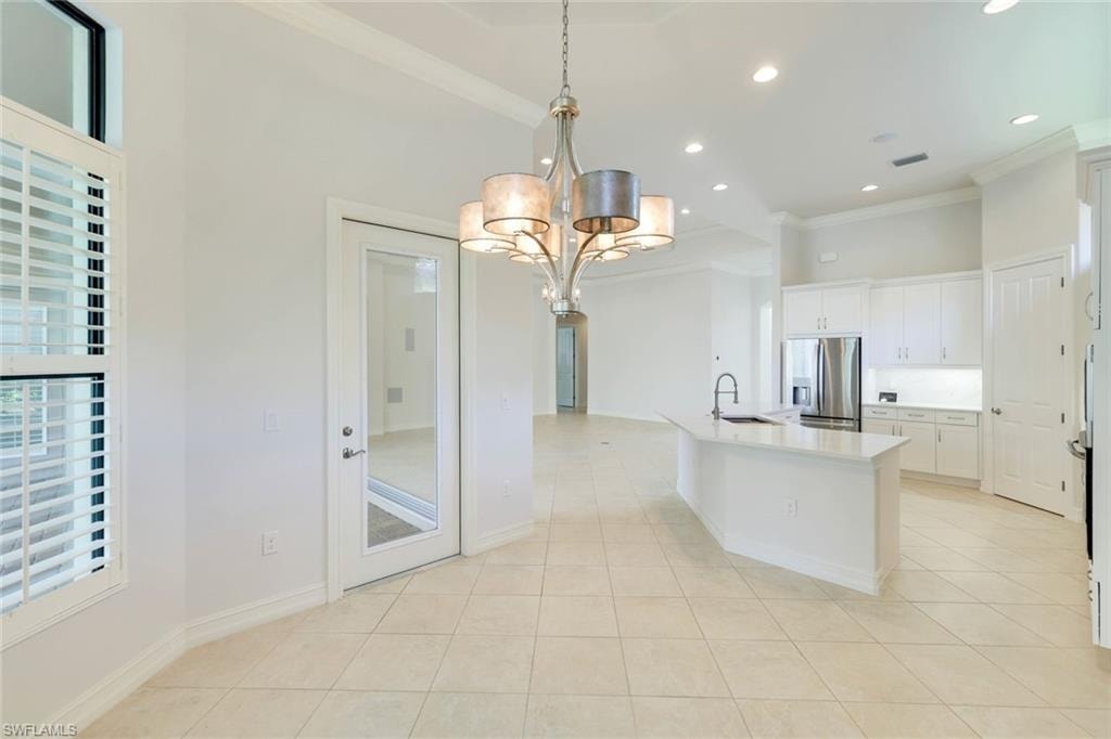 Kitchen with white cabinets, stainless steel fridge with ice dispenser, crown molding, a chandelier, and light tile patterned floors