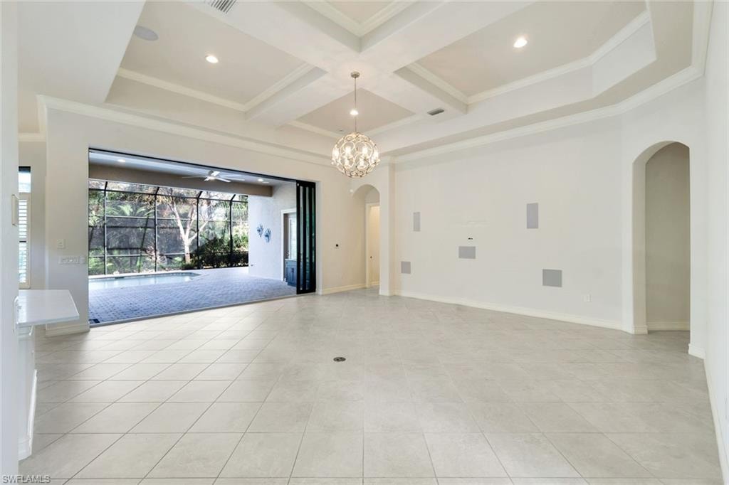 Empty room featuring arched walkways, ornamental molding, coffered ceiling, light tile patterned floors, and suspended lighting