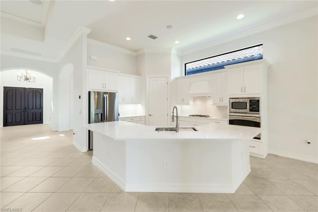 Kitchen with white cabinets, arched walkways, backsplash, light stone counters, and light tile patterned flooring