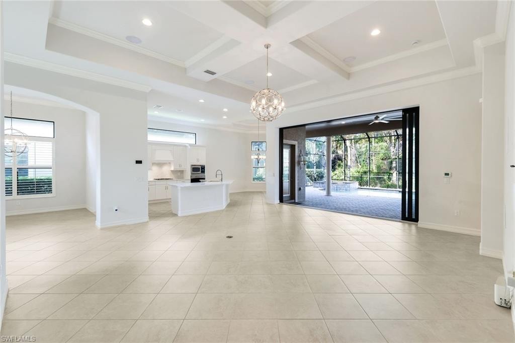 Unfurnished living room with a chandelier, coffered ceiling, ceiling fan, crown molding, and healthy amount of natural light