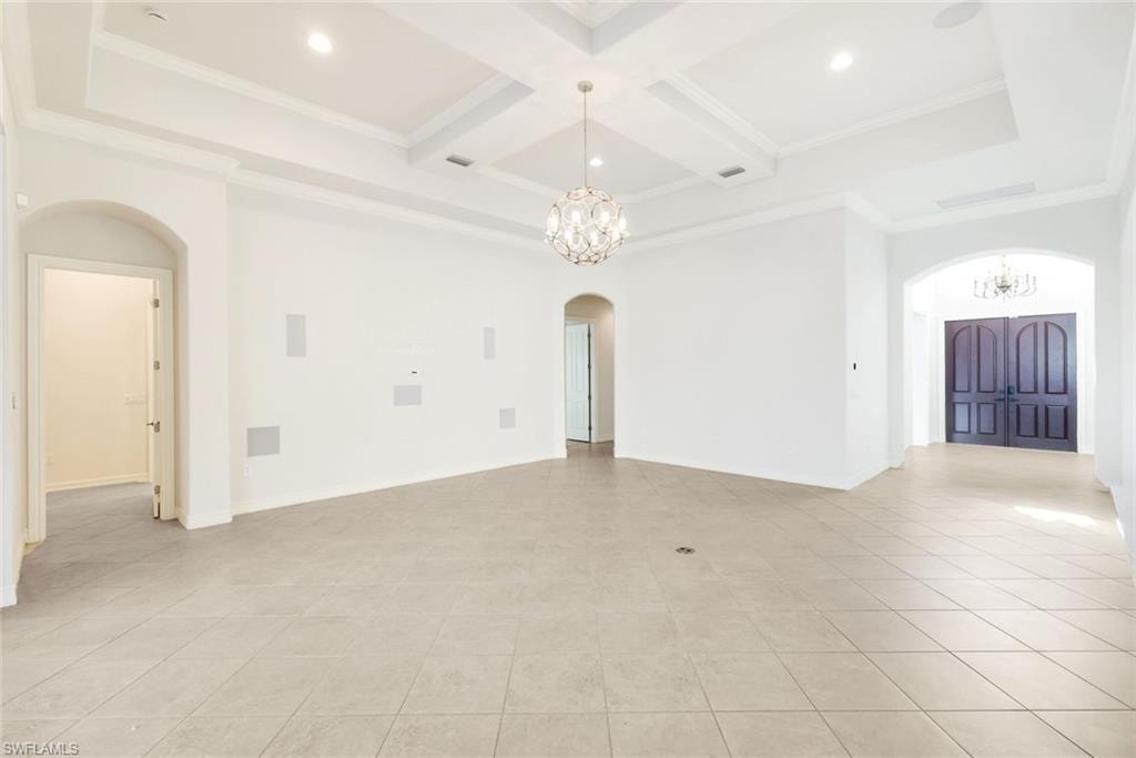 Empty room with a chandelier, arched walkways, coffered ceiling, crown molding, and light tile patterned floors
