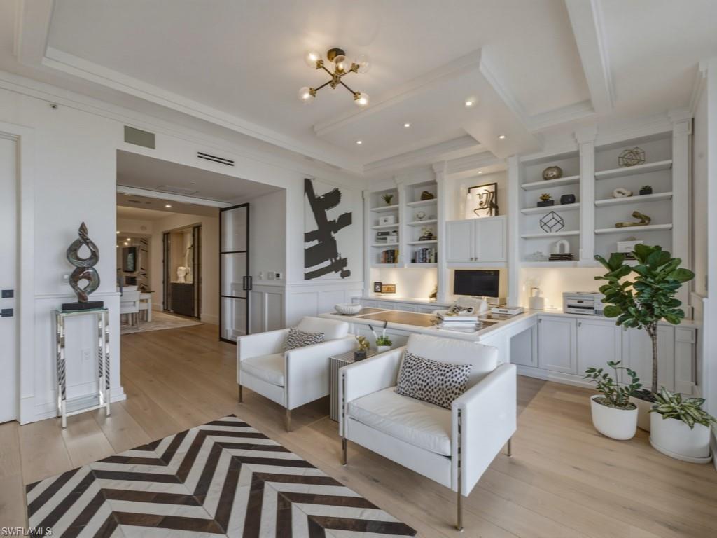 Living area featuring light wood-style flooring, crown molding, a decorative wall, wainscoting, and suspended lighting