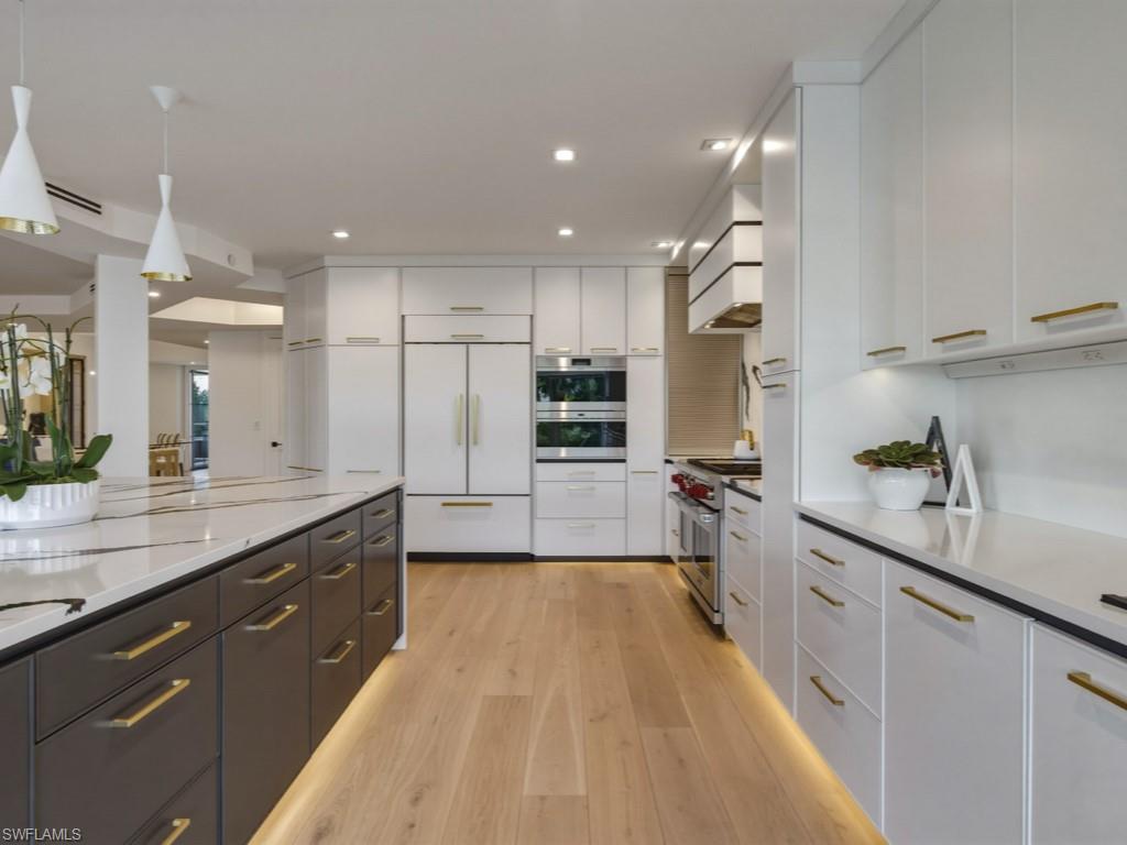 Two tone kitchen with decorative light fixtures, dual tone cabinetry, premium appliances, light wood finished floors, and light stone counters