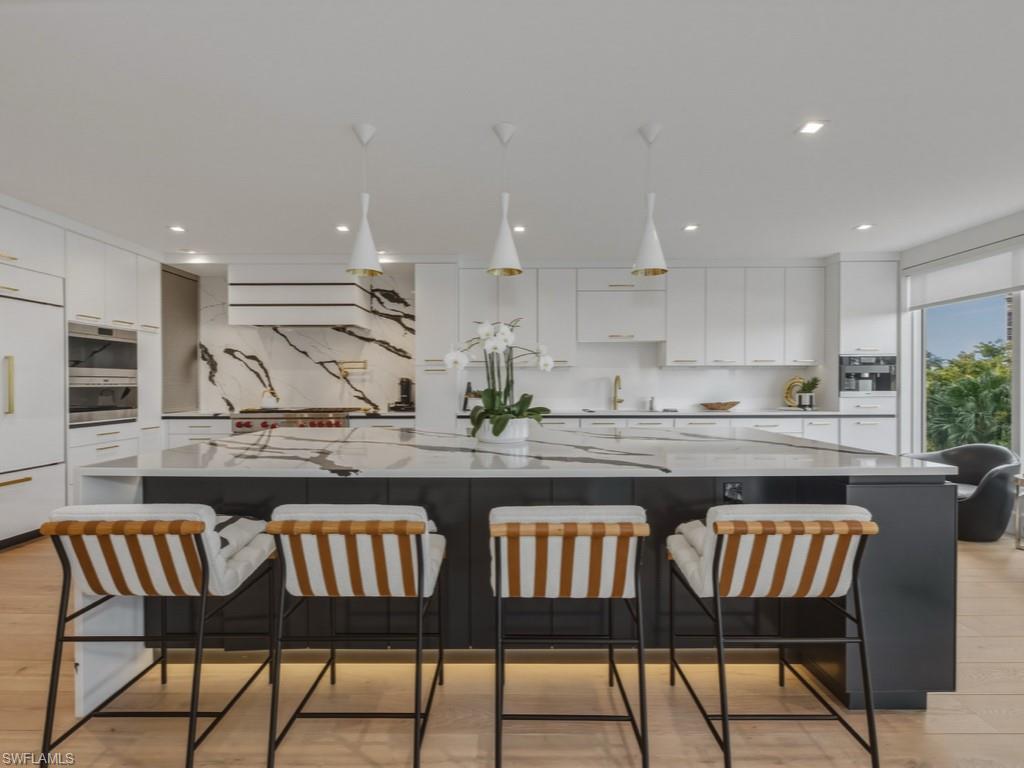 Kitchen with light wood finished floors, a spacious island, light stone counters, a breakfast bar area, and decorative light fixtures