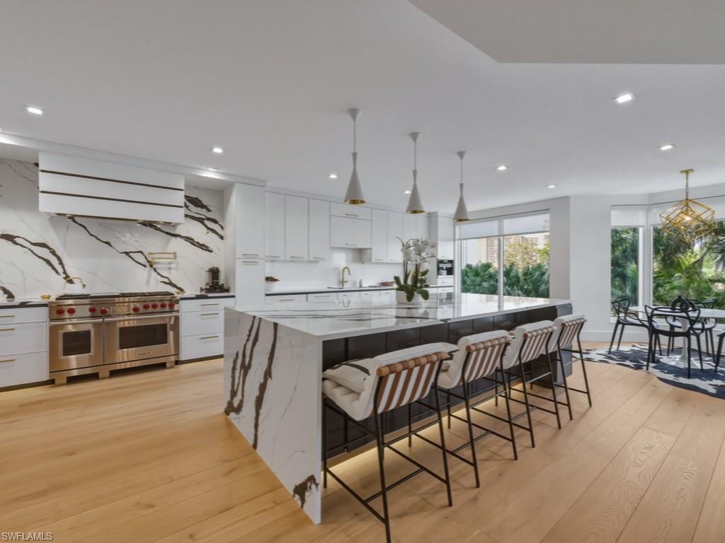 Two tone kitchen featuring Wolf gas range with two ovens, light wood-style floors, quartz countertops, a kitchen bar, and decorative light fixtures