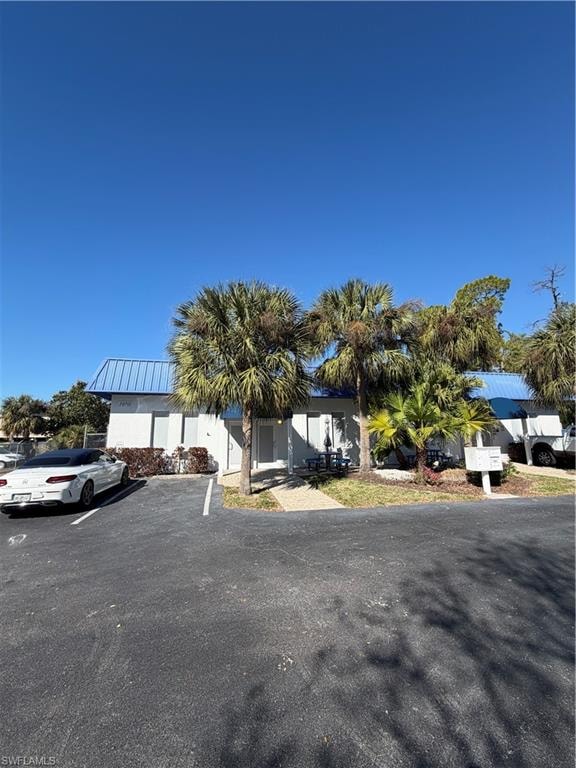 View of property hidden behind natural elements with uncovered parking and a metal roof
