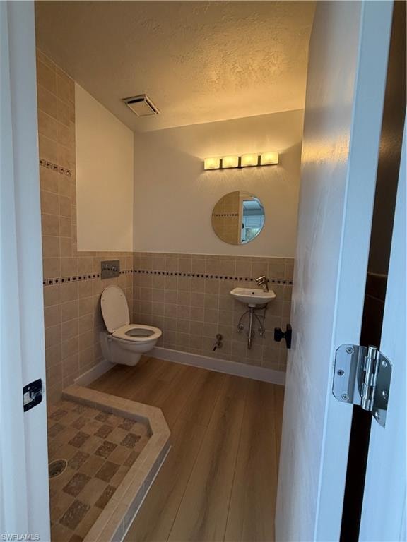 Half bath featuring tile walls, light wood finished floors, a textured ceiling, and a wainscoted wall