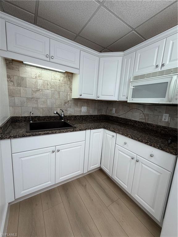 Kitchen with white cabinets, light wood finished floors, dark stone countertops, a paneled ceiling, and decorative backsplash