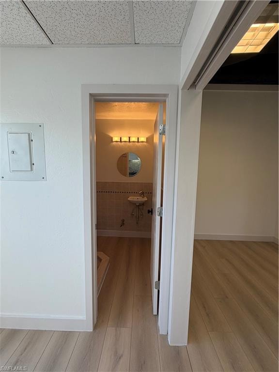 Corridor with light wood-style flooring, electric panel, and a drop ceiling