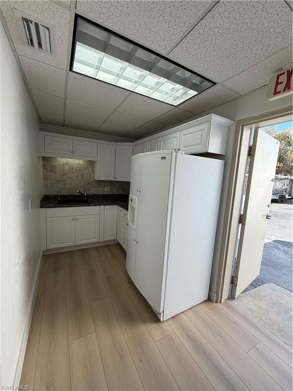 Kitchen with refrigerator, light wood-style floors, tasteful backsplash, white cabinets, and a paneled ceiling