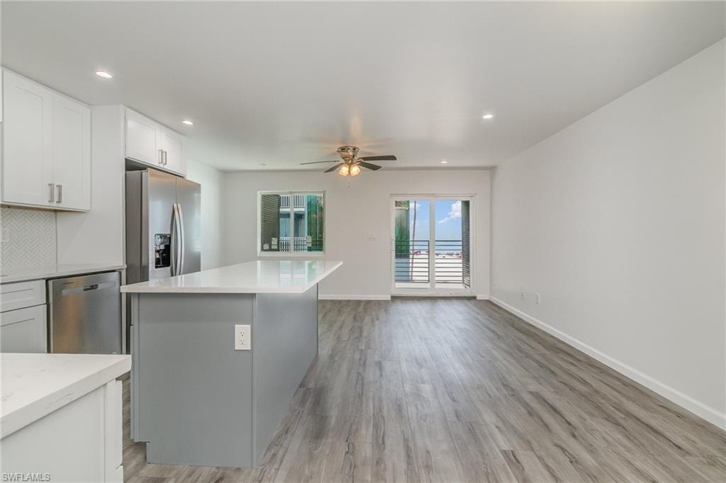 Two tone kitchen with stainless steel appliances, ceiling fan, a kitchen island, light wood-type flooring, and recessed lighting