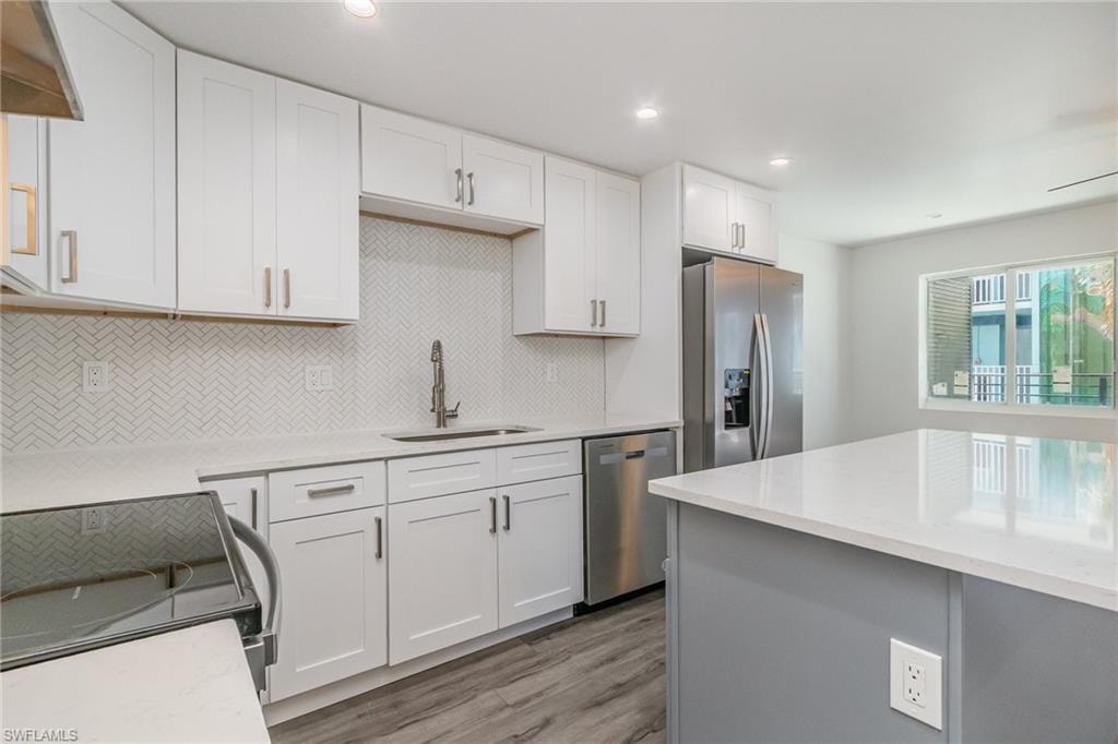 Two tone kitchen featuring stainless steel appliances, light stone countertops, light wood-style flooring, recessed lighting, and backsplash