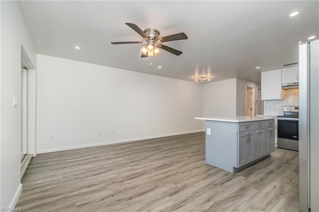 Dual tone kitchen featuring stainless steel refrigerator with ice dispenser, a kitchen island, light wood-style floors, ceiling fan, and recessed lighting