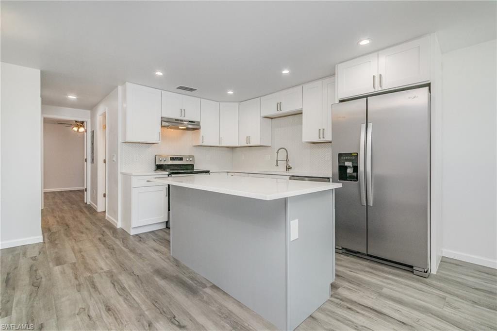 Dual tone kitchen featuring stainless steel appliances, a kitchen island, light wood-type flooring, recessed lighting, and decorative backsplash