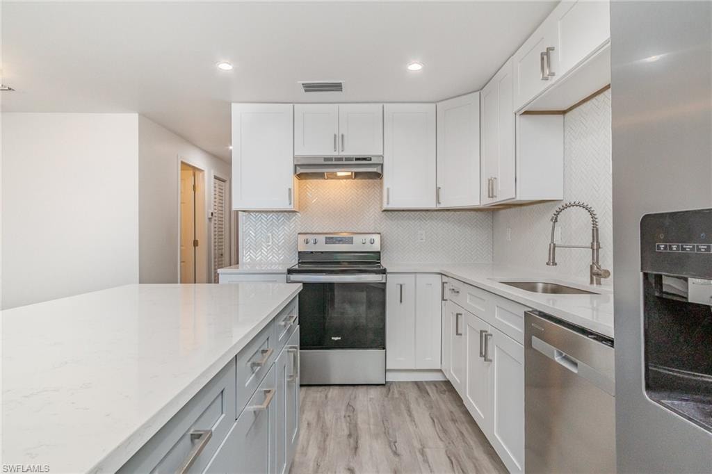 Two tone kitchen featuring stainless steel appliances, light stone countertops, recessed lighting, light wood finished floors, and decorative backsplash