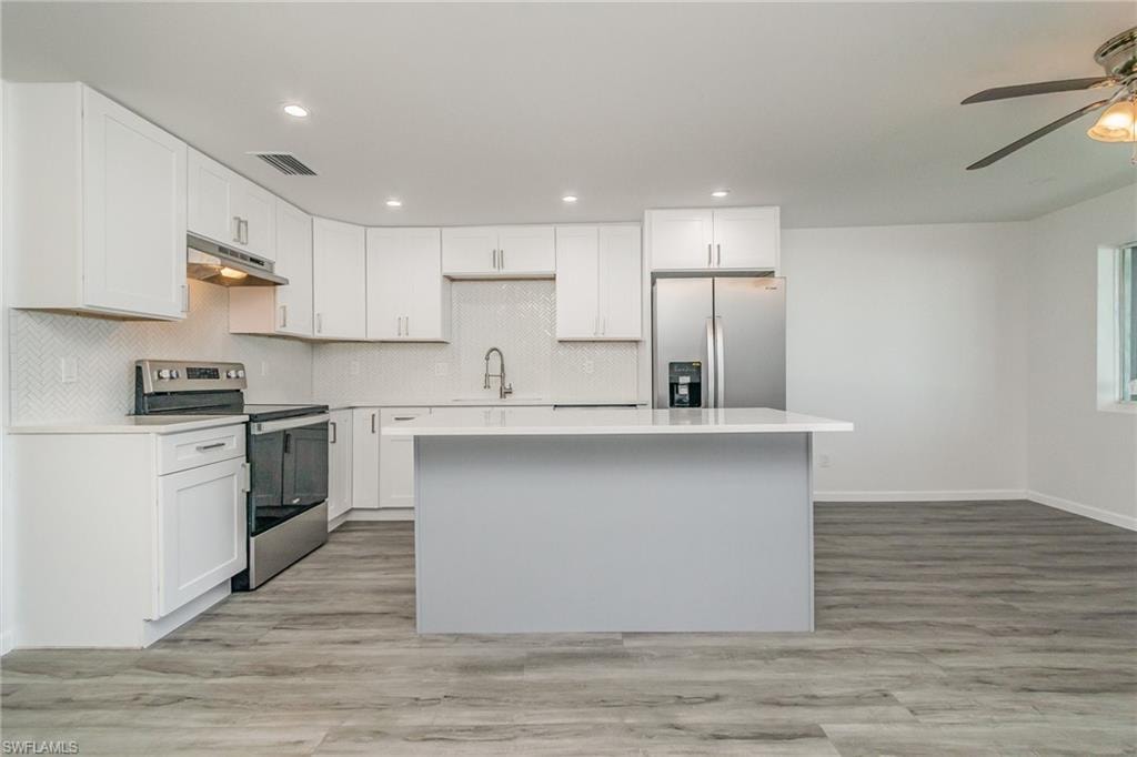 Kitchen featuring stainless steel appliances, white cabinets, a center island, a ceiling fan, and recessed lighting