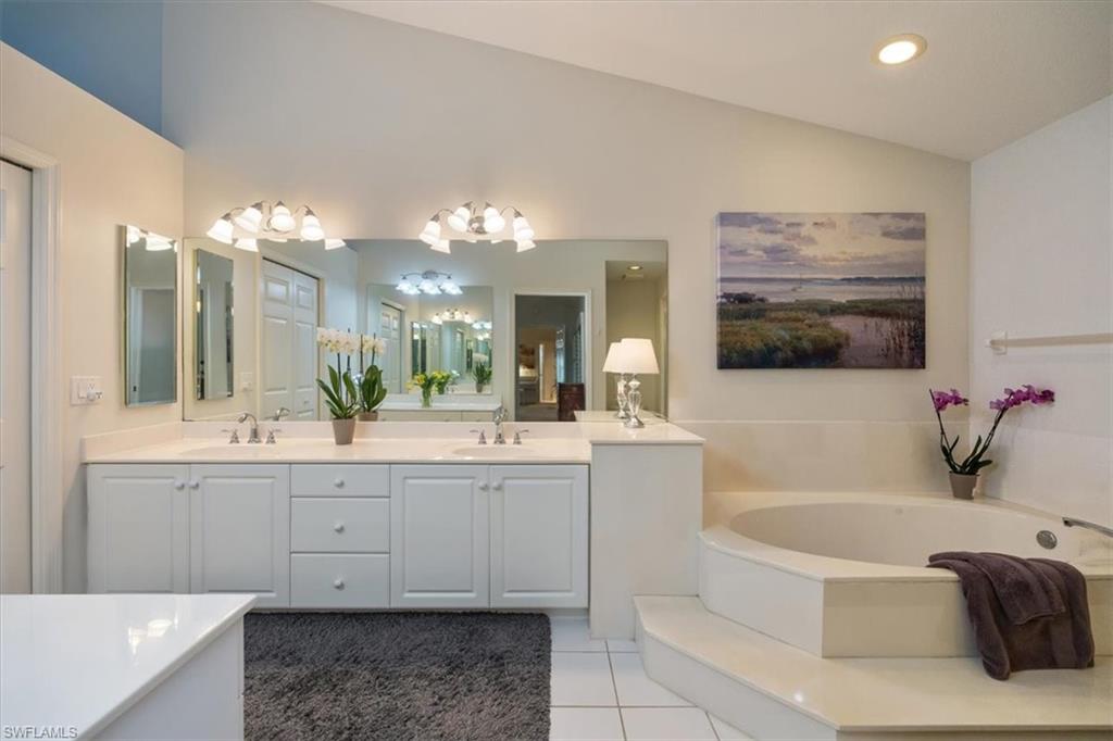 The primary bath offers dual vanities, a luxurious soaking tub, and a separate glass-enclosed shower, all opening to a spacious walk-in closet illuminated by a large window and abundant natural light.