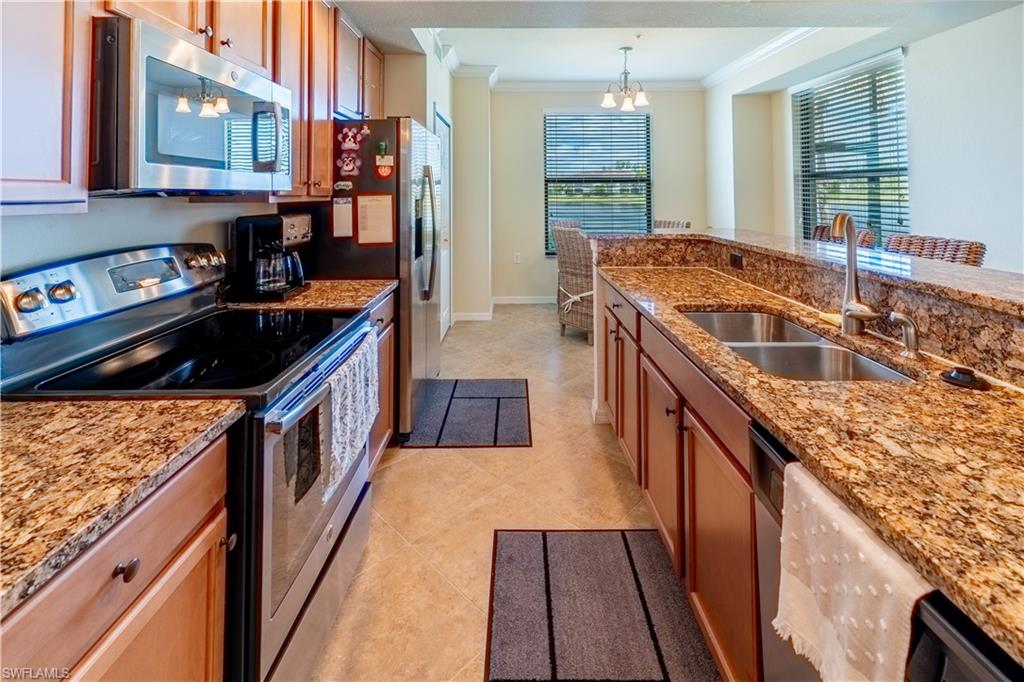 Kitchen with stainless steel appliances, hanging lights, ornamental molding, light stone countertops, and plenty of natural light