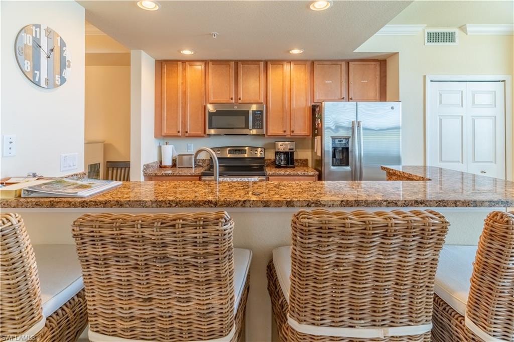 Kitchen featuring stainless steel appliances, a peninsula, recessed lighting, a breakfast bar area, and light stone countertops