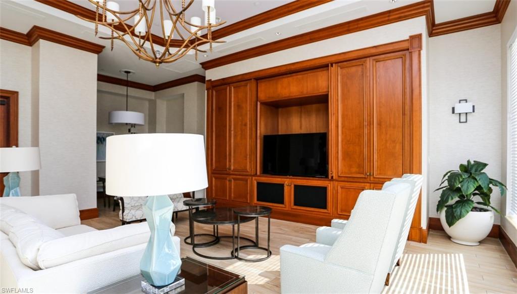 Living room featuring baseboards, light wood-type flooring, a notable chandelier, and ornamental molding