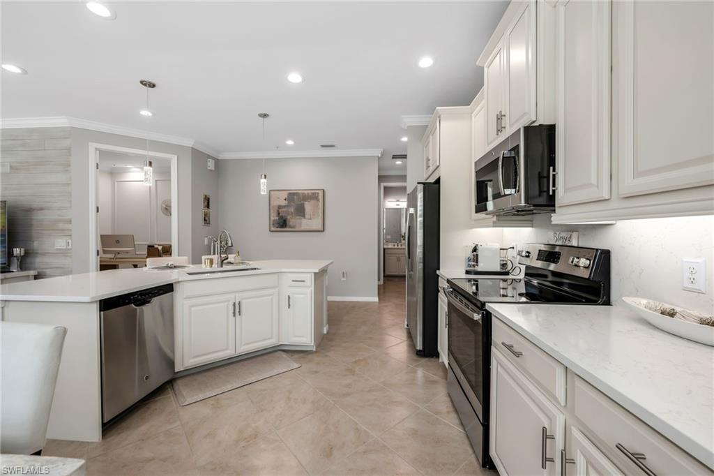 Kitchen featuring stainless steel appliances, white cabinetry, a kitchen island with sink, ornamental molding, and decorative light fixtures