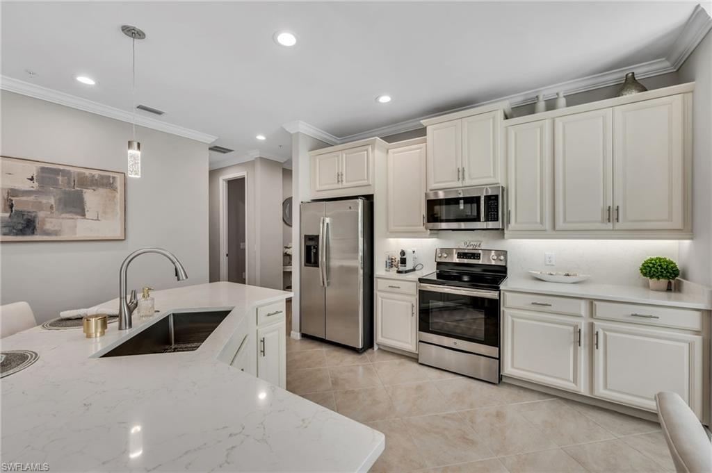 Kitchen with stainless steel appliances, ornamental molding, hanging light fixtures, light stone counters, and light tile patterned flooring