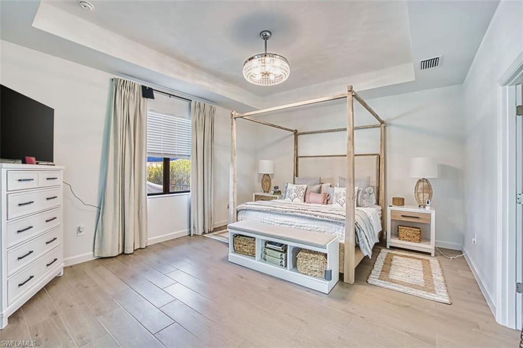 Bedroom featuring a tray ceiling, suspended lighting, and light wood-type flooring