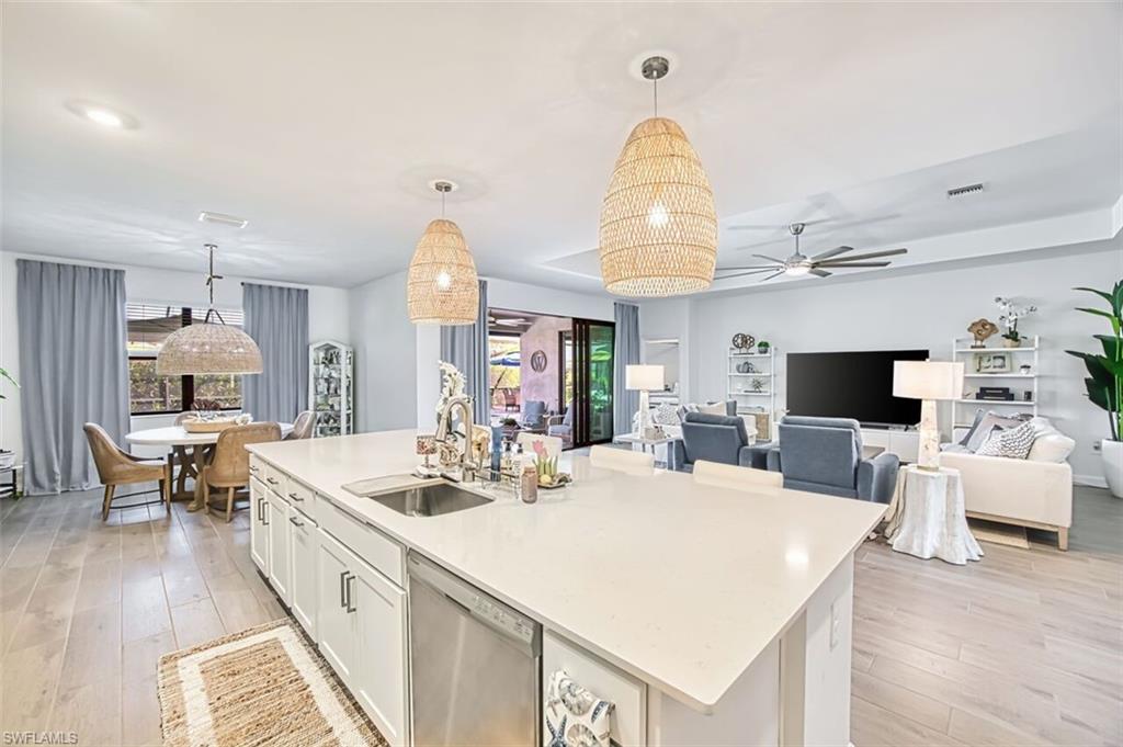 Kitchen featuring white cabinets, light wood-style flooring, stainless steel dishwasher, open floor plan, and hanging light fixtures
