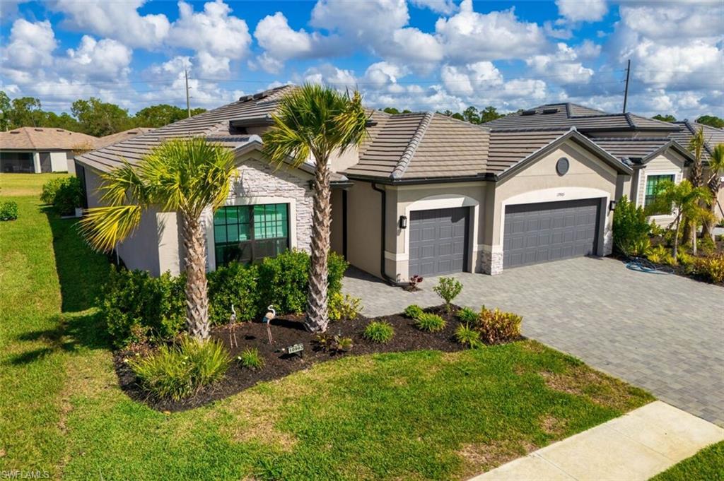 Ranch-style house with stone siding, an attached garage, decorative driveway, stucco siding, and a front lawn
