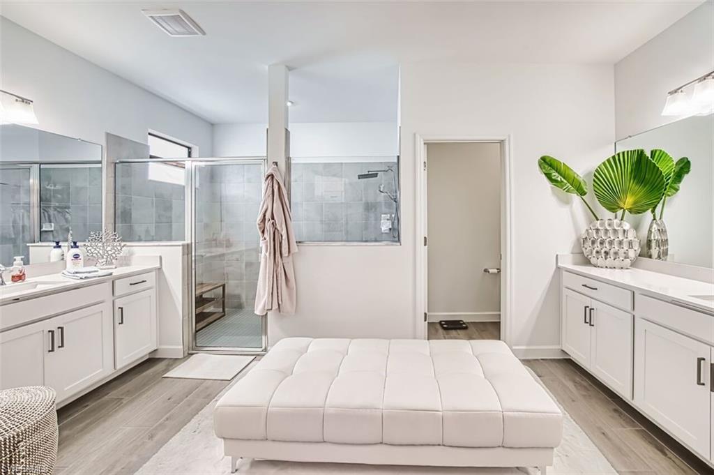 Bathroom featuring wood finish floors, two vanities, and a shower stall