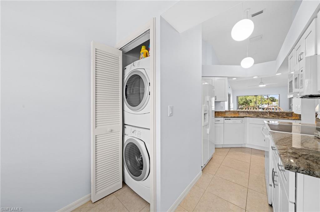 Laundry area featuring stacked washing machine and dryer, light tile patterned floors, and lofted ceiling