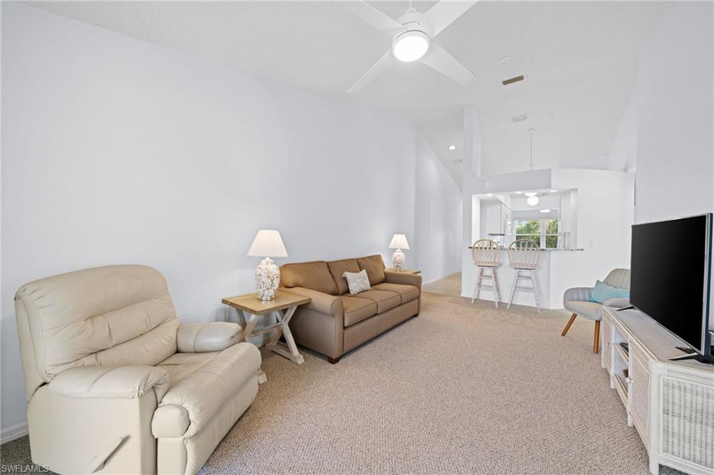 Living area featuring light colored carpet, a ceiling fan, and vaulted ceiling