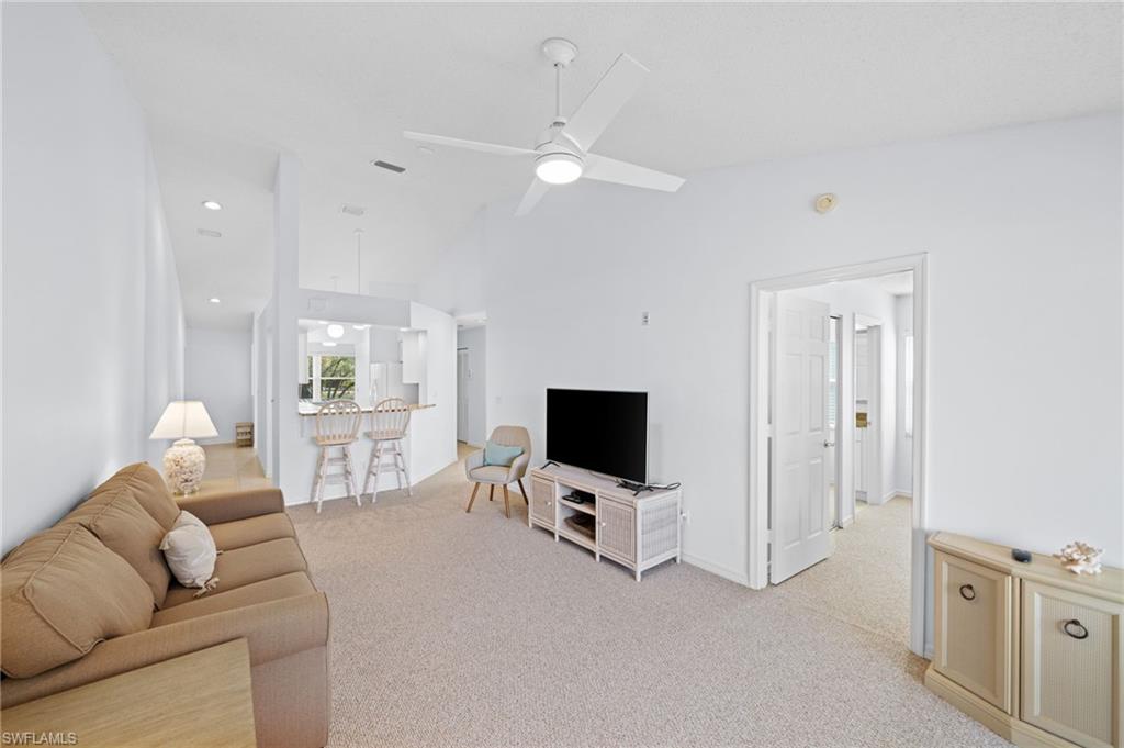 Living area with vaulted ceiling, ceiling fan, and light colored carpet