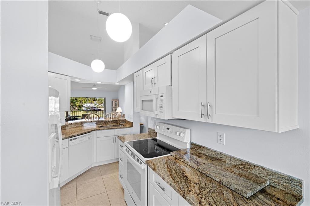Kitchen with white appliances, dark stone countertops, white cabinetry, light tile patterned flooring, and decorative light fixtures