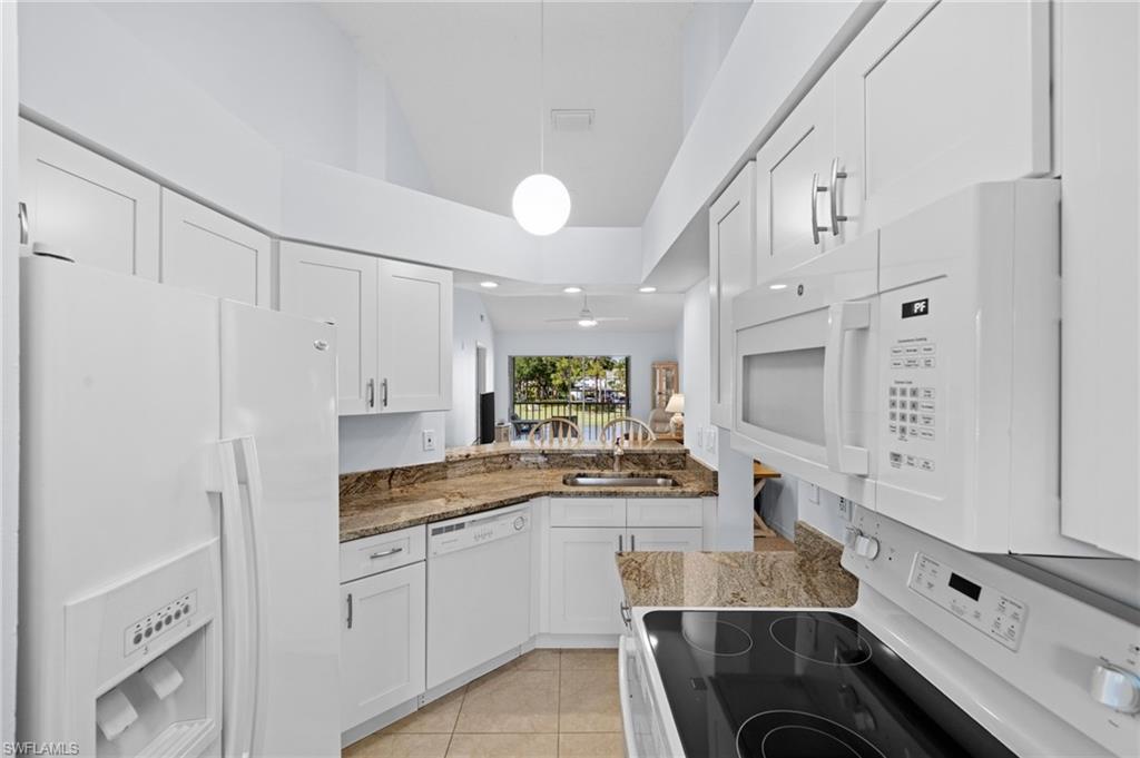 Kitchen featuring white appliances, dark stone counters, white cabinetry, light tile patterned floors, and pendant lighting