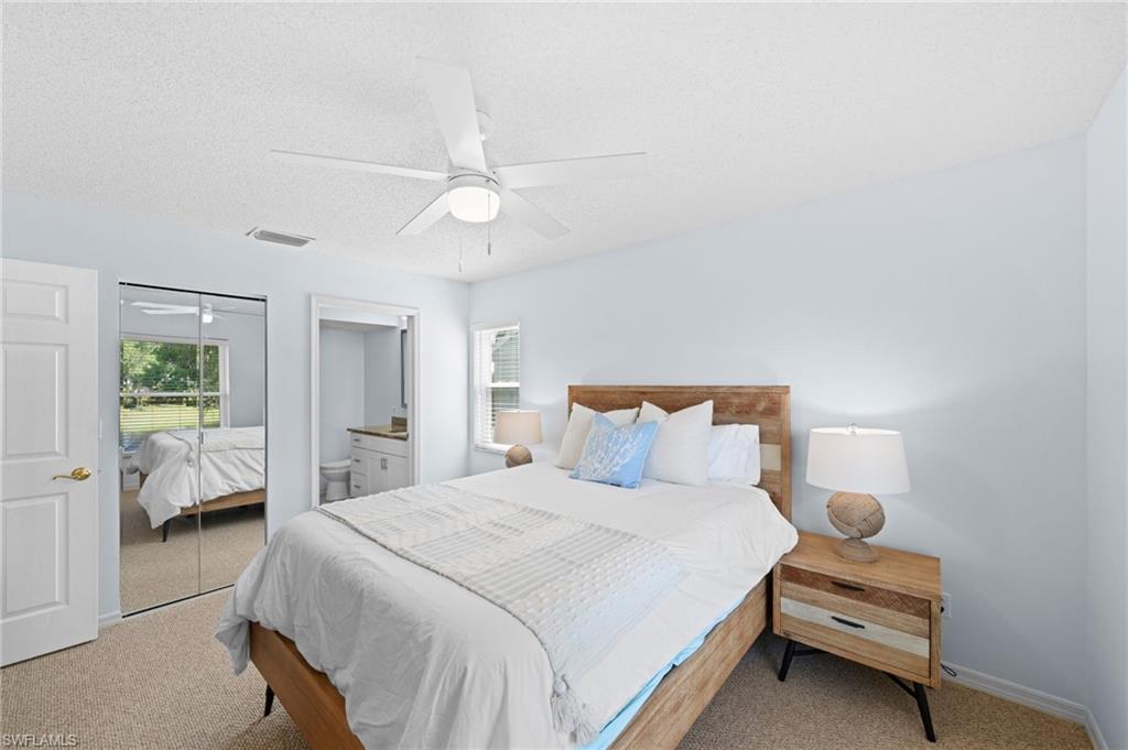 Carpeted bedroom featuring ensuite bathroom, ceiling fan, a textured ceiling, and a closet