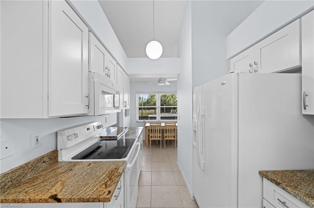 Kitchen with white appliances, white cabinets, light tile patterned floors, pendant lighting, and dark stone counters