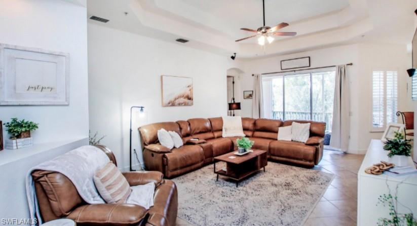 Tiled living area featuring a tray ceiling, arched walkways, and ceiling fan