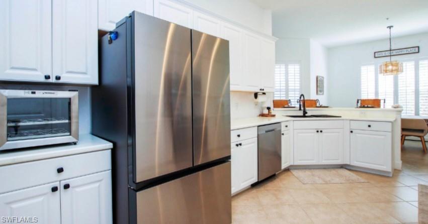Kitchen featuring stainless steel appliances, white cabinets, light countertops, and a peninsula