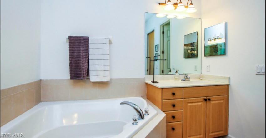 Bathroom with vanity, a garden tub, and hanging lights