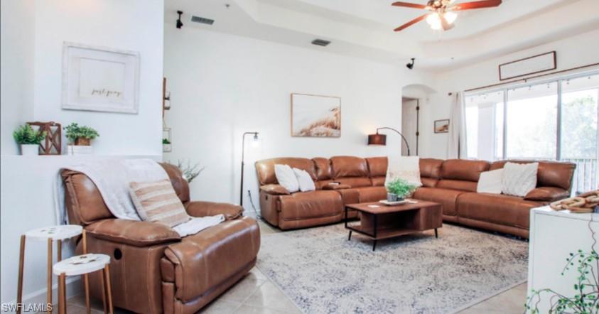 Tiled living room featuring a tray ceiling, arched walkways, and ceiling fan