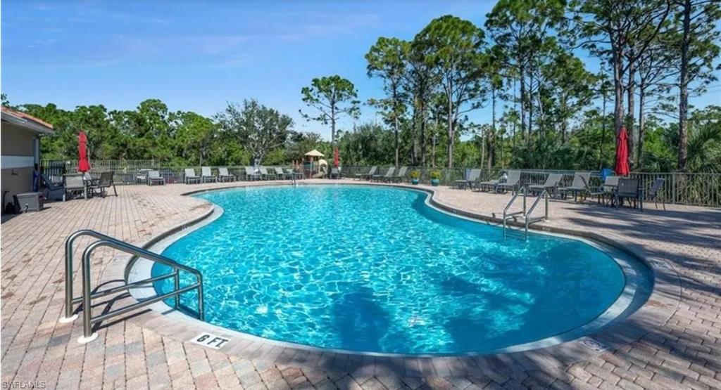 Community pool with a patio area and view of wooded area